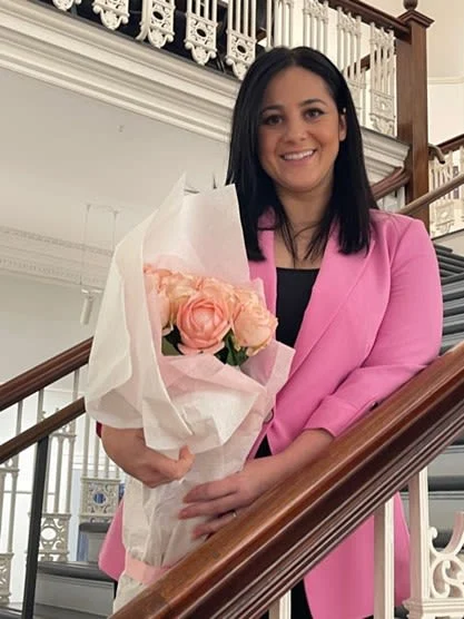 A woman with ME/CFS wearing a pink blazer while holding a bouquet of roses.