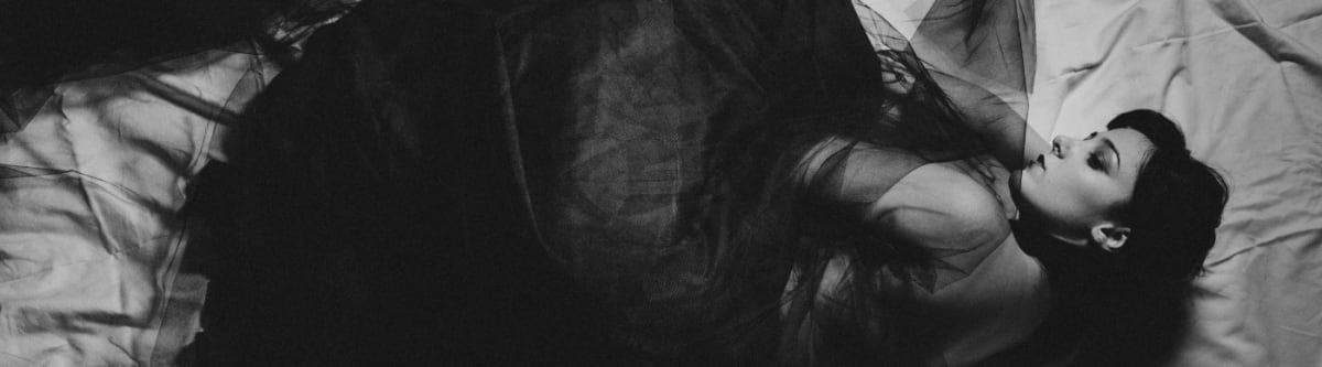 A woman with ME/CFS portrayed in a monochrome bed scene.