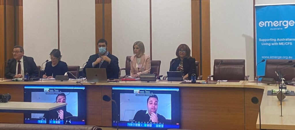 A group of people with ME/CFS sitting at a table in front of televisions.